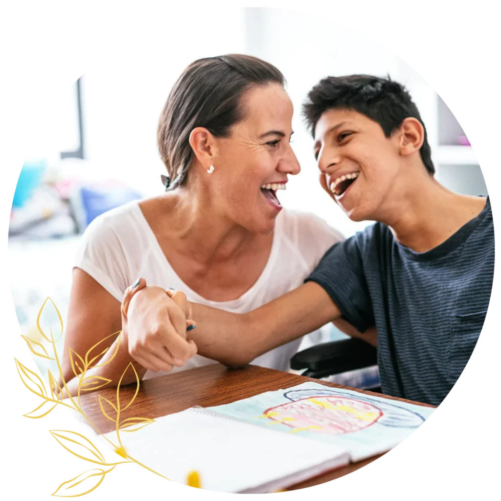 A young disabled teenage boy and his caregiver are smiling together while spending time drawing and creating art