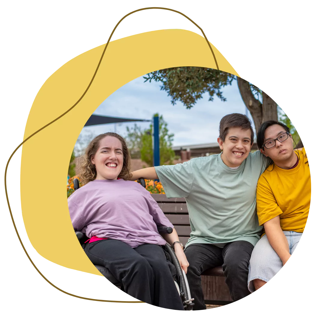 A group of 3 disabled friends are smiling together while spending time outdoors at a park